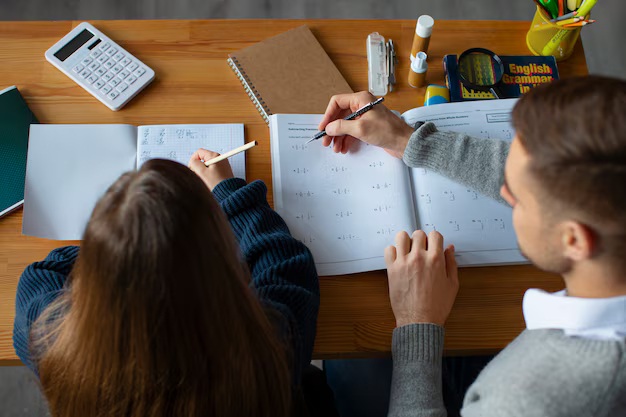 Estudiantes colaborando en tareas académicas, utilizando cuadernos y calculadora en una mesa de estudio.